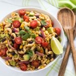 Overhead view of pasta salad with black beans, corn, avocado and tomatoes in a white bowl.
