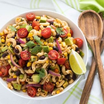 Overhead view of pasta salad with black beans, corn, avocado and tomatoes in a white bowl.