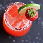 Overhead view of a strawberry margarita in a glass garnished with lime and a strawberry.