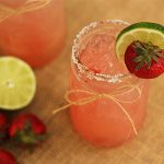A pink margarita in a mason jar garnished with strawberry and lime.