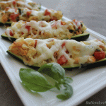 A closeup of zucchini boats with vegetables on a white serving tray.