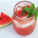 A watermelon cocktail in a mason jar garnished with a fresh mint sprig.