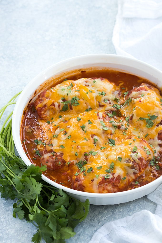 Four baked boneless chicken breasts with salsa and cheese in a white baking dish.