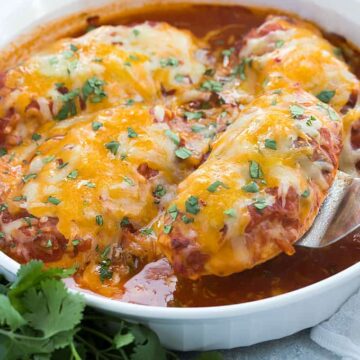 A spatula removing a baked chicken breast topped with salsa and melted cheese from a dish.