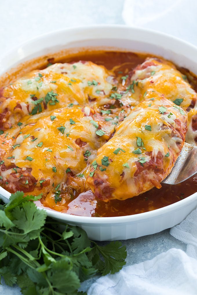 A spatula removing a baked chicken breast topped with salsa and melted cheese from a dish.