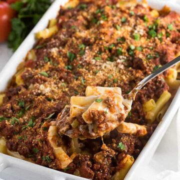 A serving spoon removing baked ziti with ground beef from a white baking dish.