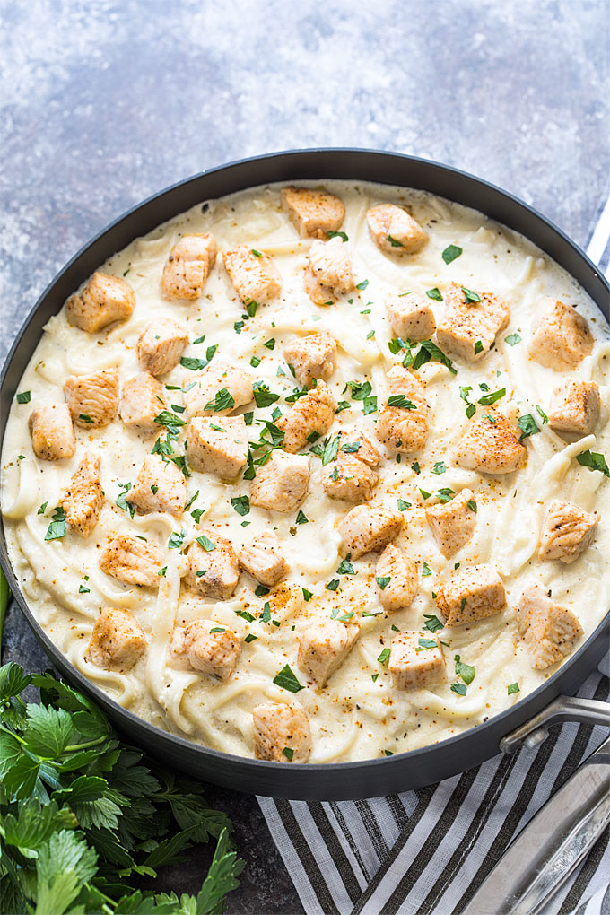 Overhead view of Cajun chicken Alfredo in a skillet by a striped napkin.