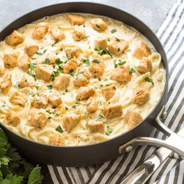Seasoned chicken pieces over fettuccine pasta with Alfredo sauce in a skillet.