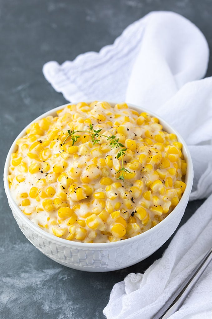 Creamed corn topped with a sprig of fresh thyme in a white bowl.