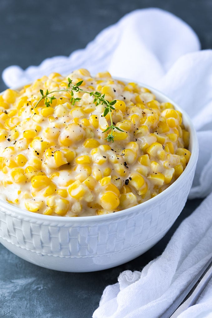 Front closeup of creamed corn garnished with a sprig of fresh thyme in a white bowl.