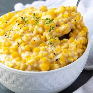 A spoon removing a spoonful of creamed corn from a white bowl.