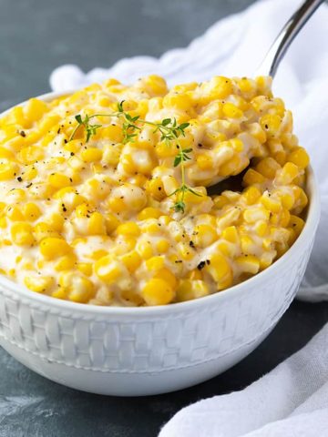 A spoon removing a spoonful of creamed corn from a white bowl.