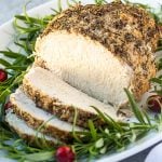 A sliced turkey breast garnished with rosemary and cranberries on a white platter.