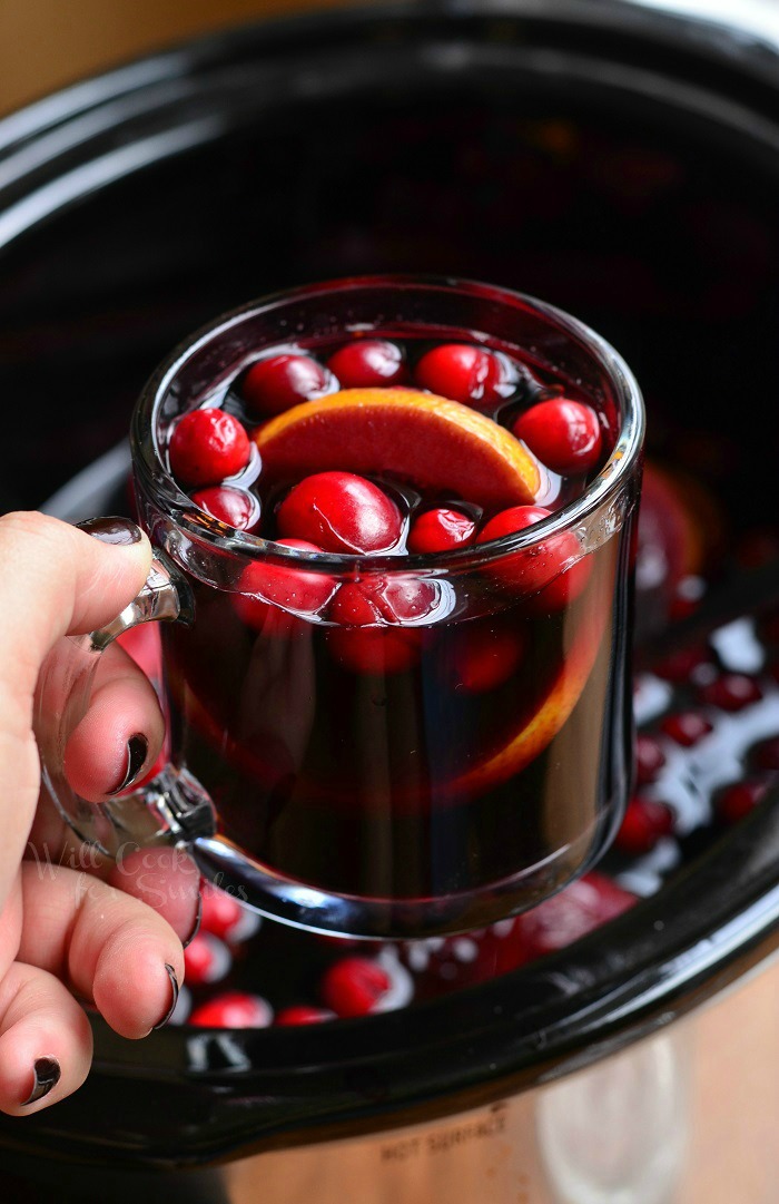 A hand holding a mug of sangria with cranberries and orange slices.