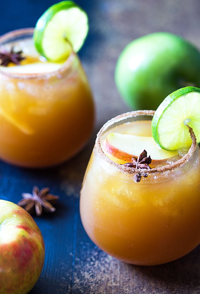 Two glasses of cider margaritas garnished with sliced apple, lime and a star anise.