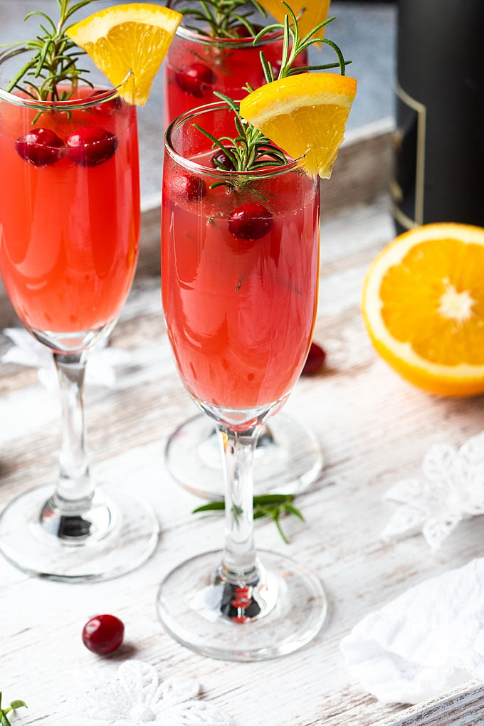 Front view of three garnished cranberry orange mimosas on a white wood surface.