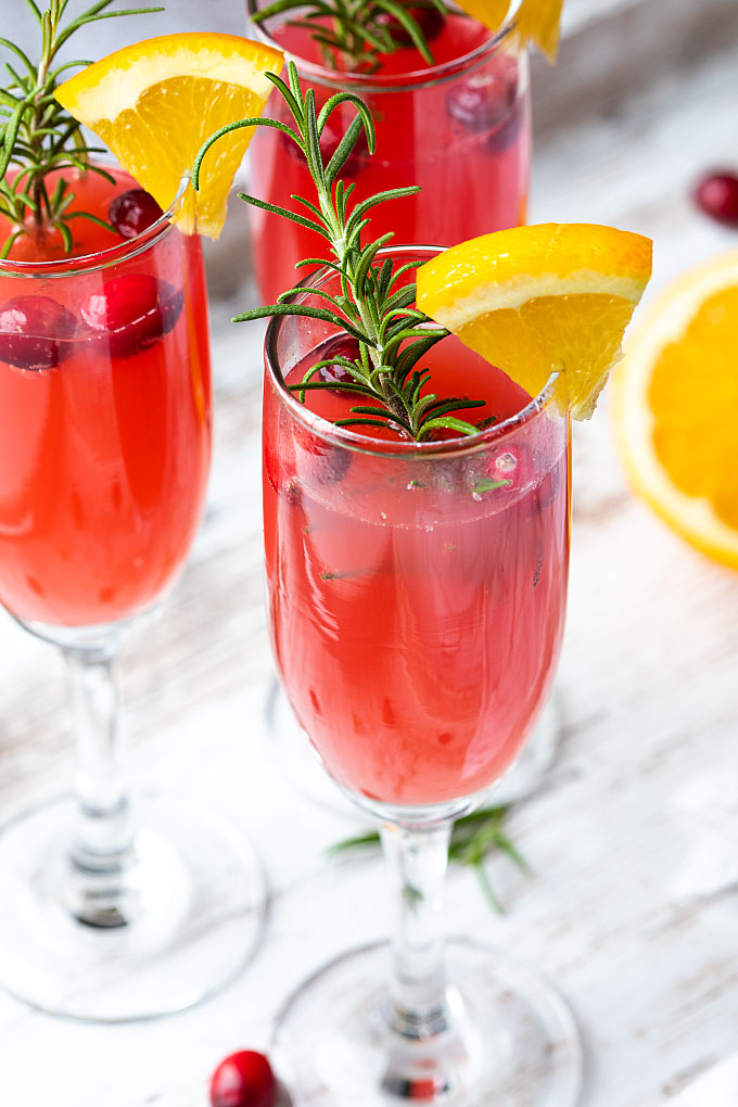 Three mimosas garnished with rosemary, cranberries and an orange slice.