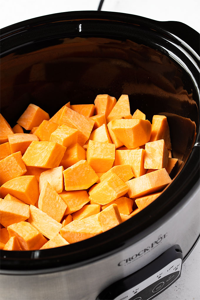 Cubed raw sweet potatoes in an oval slow cooker.