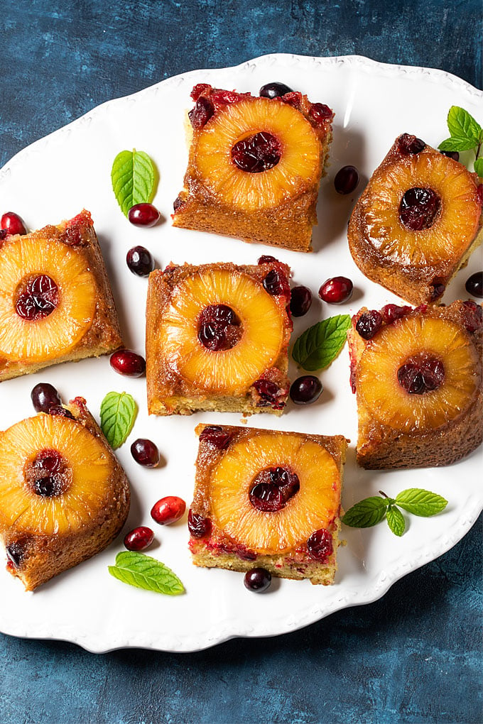 Overhead view of slices of pineapple upside-down cake with cranberries on a white platter.