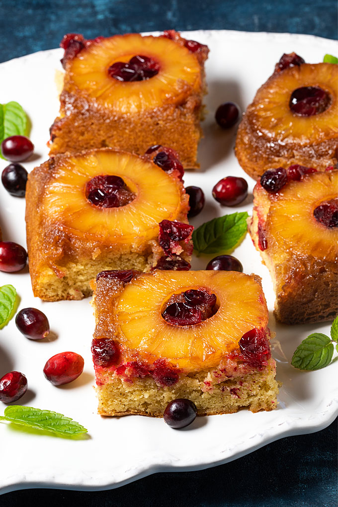 Closeup view of sliced pineapple cranberry upside-down cake on a white platter.