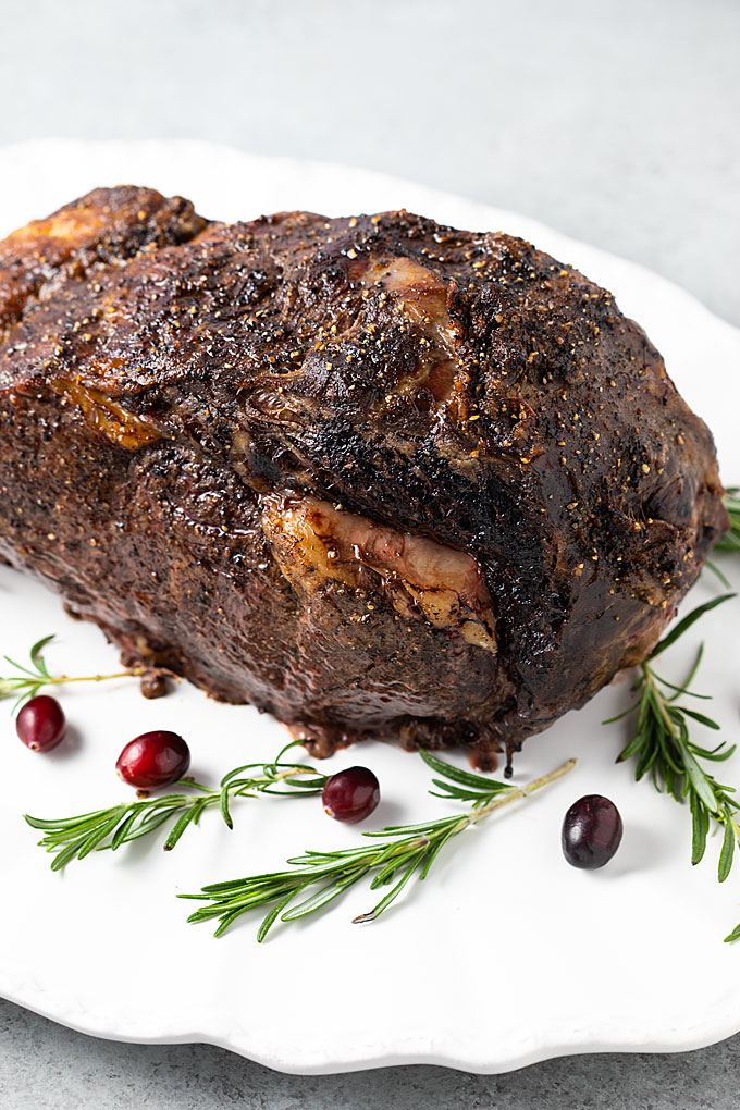 A boneless prime rib on a white serving platter with rosemary sprigs and cranberries.