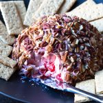 Cherry Cheese Ball on a black plate with a cheese knife and graham crackers.