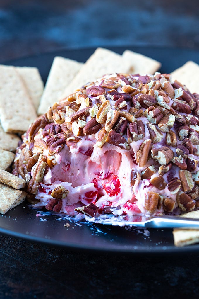 Cherry Cheese Ball on a black plate with a cheese knife and graham crackers.