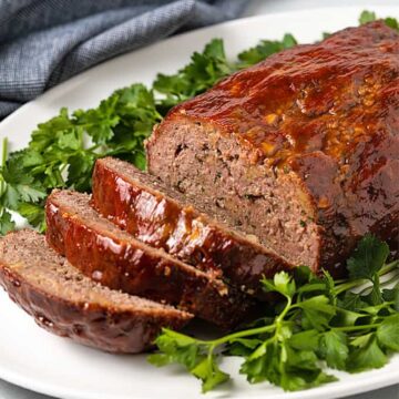 Sliced Classic Meatloaf on an oval white platter with parsley and a denim napkin.