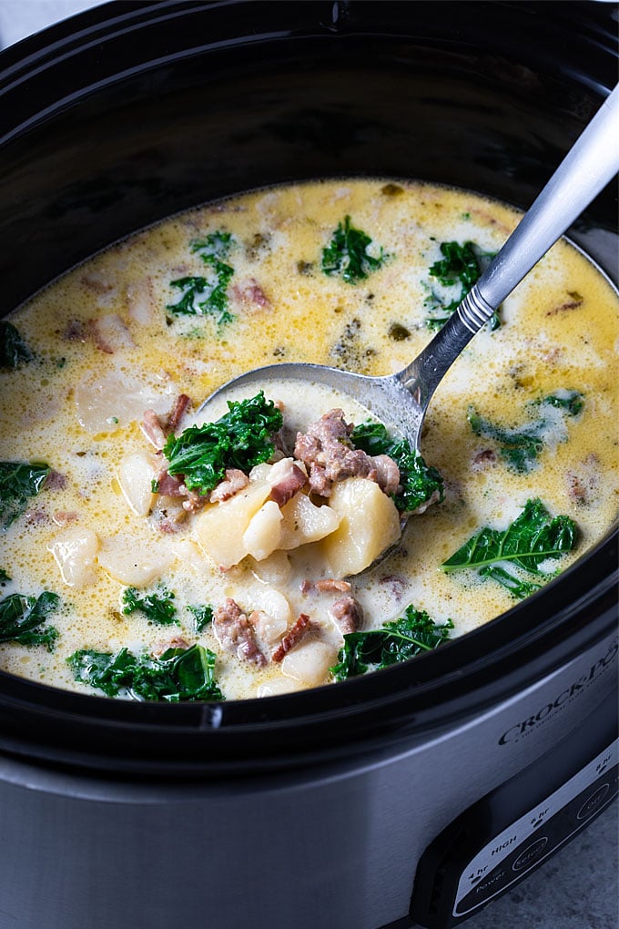 Zuppa Toscana soup in a crock pot slow cooker with a ladle.