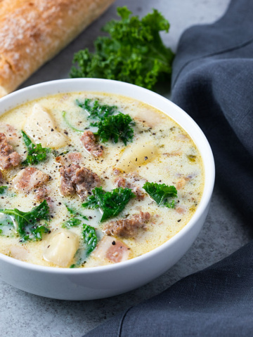 Crock Pot Zuppa Toscana soup in a white bowl with French bread and a dark grey napkin.