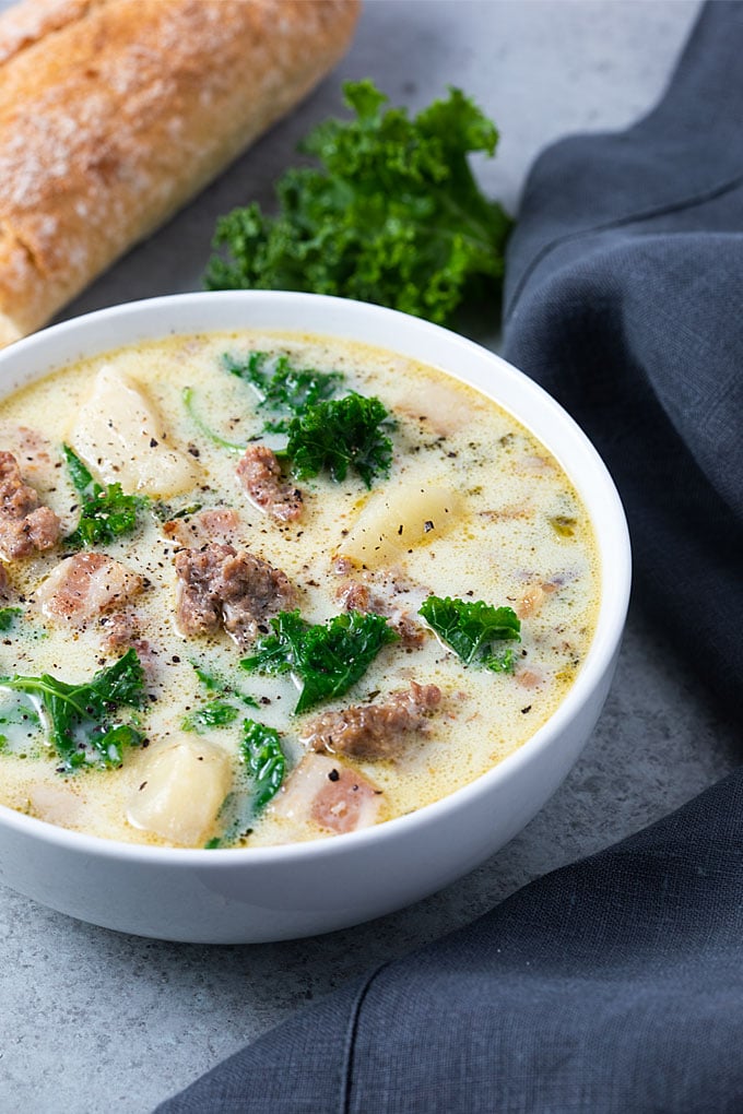 Crock Pot Zuppa Toscana soup in a white bowl with French bread and a dark grey napkin.