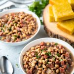 Black-eyed peas and ham in two white bowls. with two spoons