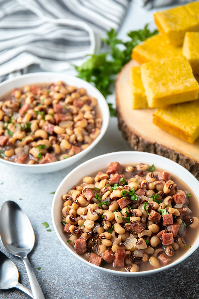 Black-eyed peas and ham in two white bowls. with two spoons