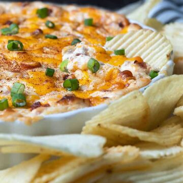 Loaded Baked Potato Dip spread on a potato chip in a white dish.