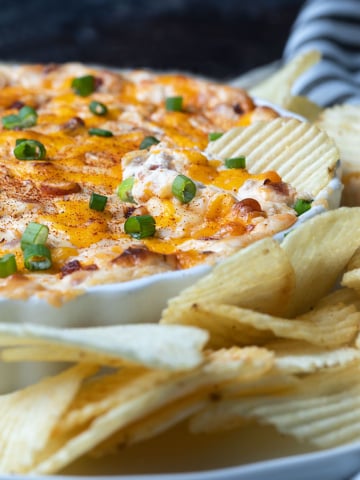Loaded Baked Potato Dip spread on a potato chip in a white dish.