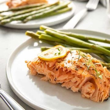 Maple glazed salmon topped with lemon slices and asparagus on a round white plate.