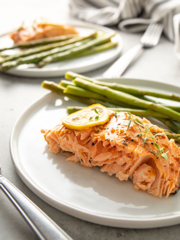 Maple glazed salmon topped with lemon slices and asparagus on a round white plate.
