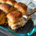 Baked Reuben sliders in a glass dish with a wooden spatula.