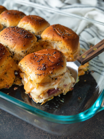 Baked Reuben sliders in a glass dish with a wooden spatula.