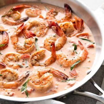 Shrimp in a tomato basil cream sauce in a skillet beside a white kitchen towel.
