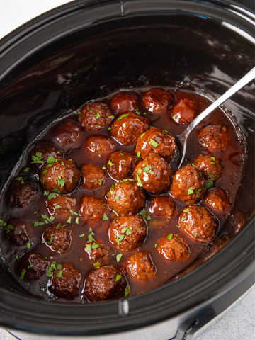 Bourbon meatballs topped with fresh chopped parsley in an oval slow cooker.