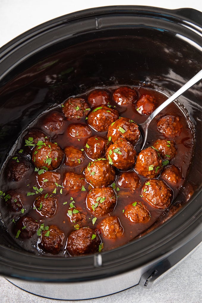 Bourbon meatballs topped with fresh chopped parsley in an oval slow cooker.