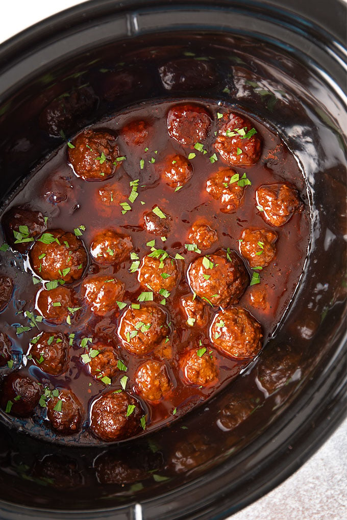 Bourbon meatballs sprinkled with chopped parsley in a black oval slow cooker.