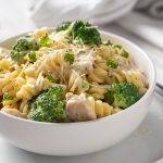 Front view of Chicken and Broccoli Alfredo in a round white bowl beside a fork and white kitchen towel.