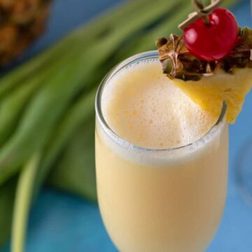 A pineapple cream mimosa in a champagne flute garnished with a pineapple wedge and cherry.