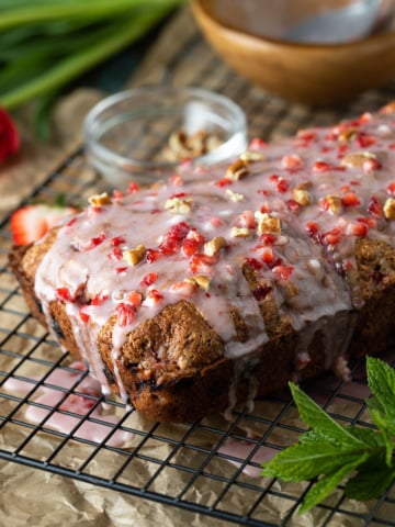 A loaf of glazed strawberry pecan bread on a black wire rack beside a sprig of fresh mint.