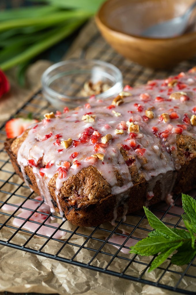 A loaf of glazed strawberry pecan bread on a black wire rack beside a sprig of fresh mint.
