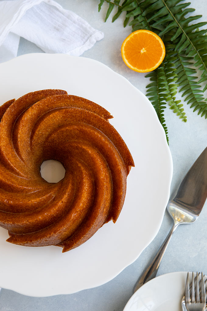 Overhead shot of a spiced orange rum cake on a round white platter beside a cake serving knife.