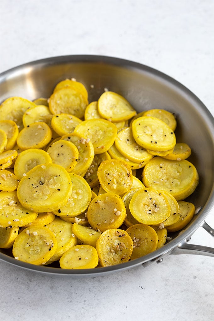 Sauteed sliced yellow squash in a stainless steel skillet.