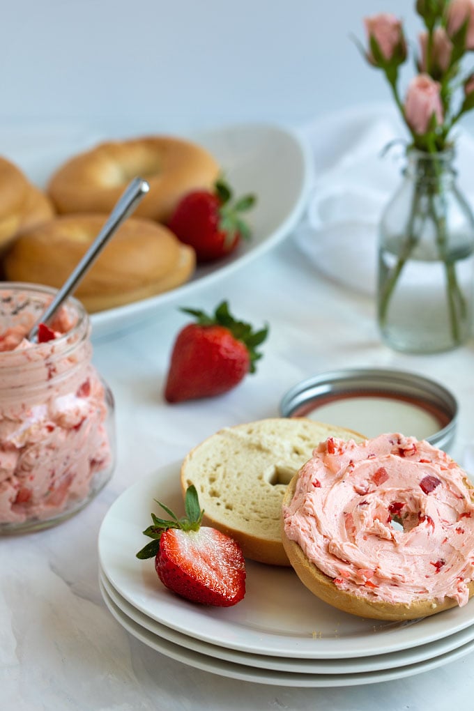 A bagel spread with strawberry honey butter on a round white plate.